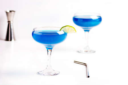 Sparkling blue glitter drinks in lime decorated cocktail glasses are on a white table.の写真素材