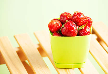 Ripe red strawberries lies in a light green bucket on a yellow background.の写真素材
