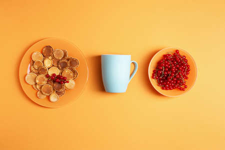 Homemade mini pancakes in an orange plate on an orange background, next to it is a blue ceramic mug...