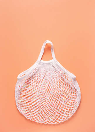 Mesh bag rests on a peach surface, zero waste concept, vertical orientation.の写真素材