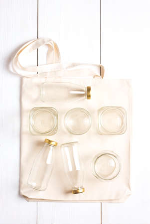 Waste-free shopping set. A reusable woven bag rests on a white surface with glass bottles and jars...