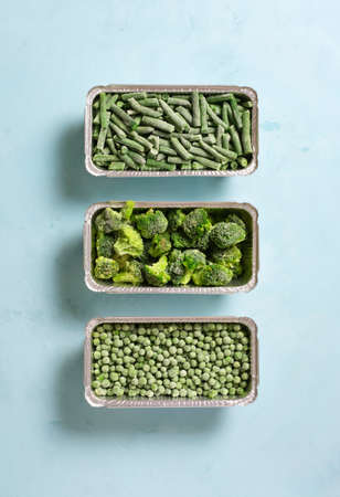 Frozen green vegetables on blue background, flat lay, vertical orientation