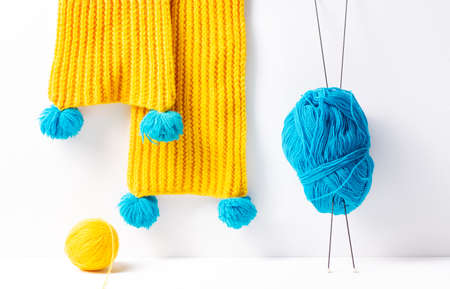 Yellow knitted scarf, next to blue and yellow yarn on a white background. Knitting hobby concept, horizontal orientation.の写真素材