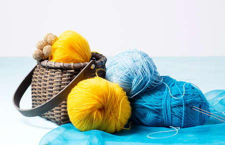 Skeins of blue, blue, yellow yarn lie on a light-blue background, next to it there is a wicker basket with yellow yarn. Hobby knitting, horizontal orientation, close-up, selective focus on blue skein.の写真素材