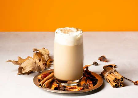 Traditional autumn pumpkin spice latte in a glass on a metal tray with spices. Close-up, orange...