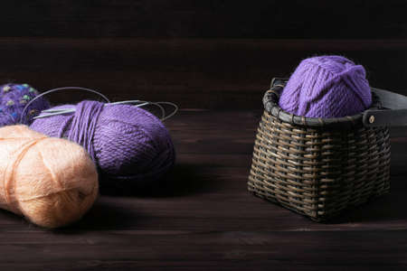 This photo shows a wicker basket with purple yarn and skeins of wool on a dark wooden background. Handicraft and hobby concept.の写真素材