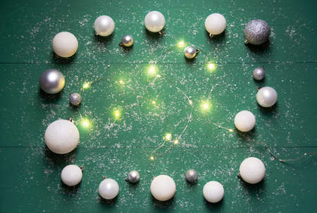 Christmas composition white and gray balls with a burning garland on a green wooden background with snow. Horizontal orientation, flat layの写真素材