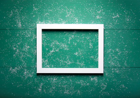 A white wooden frame lies on a green wooden background strewn with snow.の写真素材