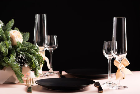 Beautiful table setting for a celebration for two, black plate and glasses, flower arrangement on a black background, side view, copy space, horizontal orientationの写真素材