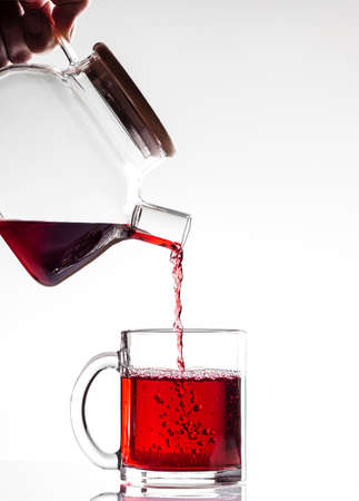 Red tea is poured into a beautiful transparent mug from a glass teapot on a white background, close-up, vertical orientationの写真素材