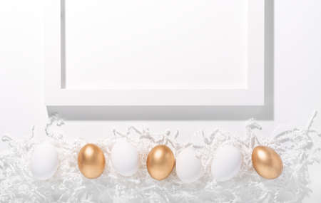 White and gold Easter eggs on a white background, next to a wooden frame for text, horizontal orientation, copy spaceの写真素材