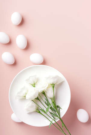 The concept of Easter table setting, white flowers lie on a white plate, next to white eggs on a powdery background, vertical orientation, copy spaceの写真素材