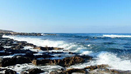 rocky shore of the blue sea, waves, white foamの写真素材