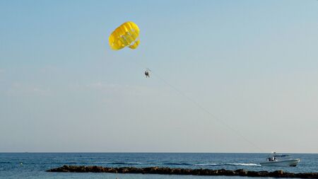 Parasailing, people flying on a yellow parachute behind a boat in the sea.の写真素材