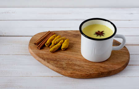 Cup of turmeric golden milk served with spices âcinnamon and star anise on white wooden background.の写真素材