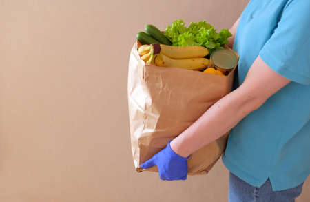 Volunteer in medical gloves delivers food in paper bag during virus outbreak, coronavirus pandemic....