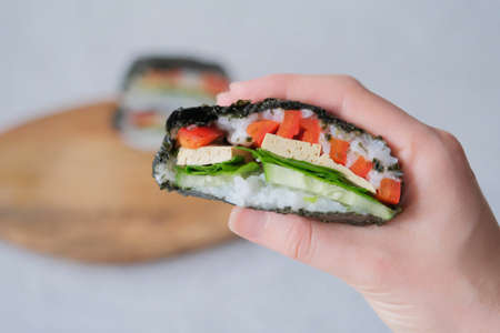 The hand of young woman, holding onigirazu, vegan sushi sandwich with vegetables (cucumber, pepper,...