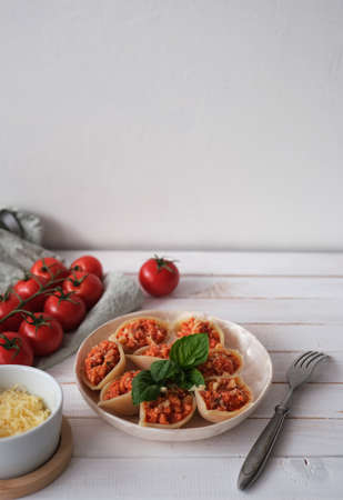Italian pasta Conchiglioni stuffed with bolognese sauce and sprinkled with cheese on white wooden table. Served with basil. Selective focus, side view. Copy space.の写真素材