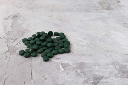 Green chlorella tablets on gray concrete background. Chlorella is a single-celled green algae, it is used to make nutritional supplements and medicine. Side view, selective focus, copy space.の写真素材