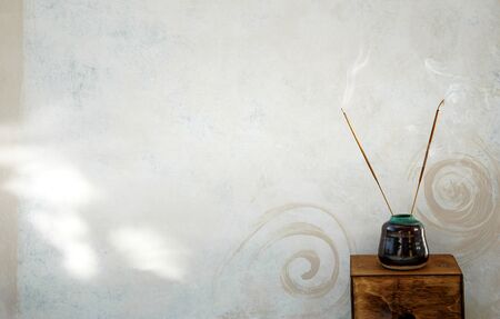 Incense burning next to a rustic spa wall painted with spirals.の写真素材