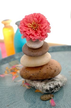 A stone carin/tower in a basin topped by a flower with spa bottles in the background.の写真素材