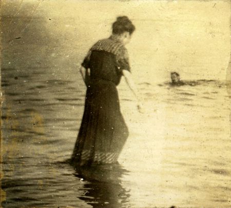 Vintage woman wades in towards a swimming man. Circa 1910. Photo very old with many scratches, fading. and solarizing qualities.の写真素材