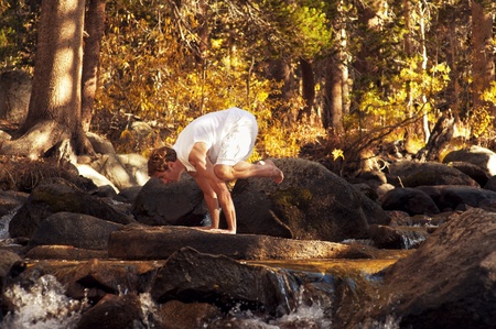 Man in yoga posture outdoors in a forest mountain river 