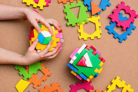 The child's hands are holding puzzle sorters in the form of cubes with details of different geometric shapes and puzzles on the table. Top view. Leisure of the child in confinementの写真素材
