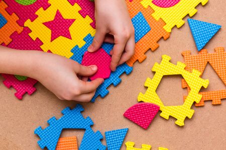 The child's hands put the item in a color puzzle with details of different geometric shapes on the table. Leisure of the child in confinement. Table game. Top viewの写真素材