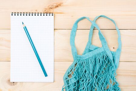 The concept of online grocery shopping without leaving home. Notepad for shopping list and string bag on a wooden table. Top viewの写真素材