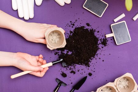 Home gardening concept. Children's hands work with the soil with a garden tool, signboards for plants, paper pots and gloves. Top viewの写真素材
