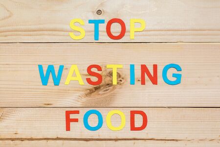 Stop wasting food. The inscription of letters cut out of color cardboard on a wooden background. Food waste conceptの写真素材