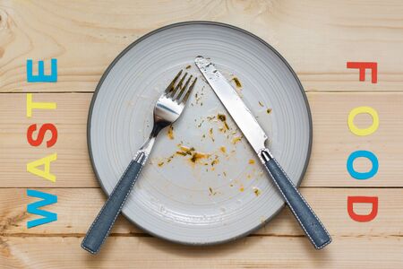 Stop wasting food. Dirty dinner plate and cutlery and the words "food waste" on a wooden background. Food waste conceptの写真素材