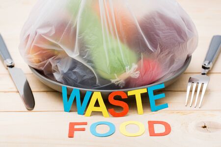 Stop wasting food. A bag of food waste on a plate and cutlery on a wooden table. Food waste concept.の写真素材