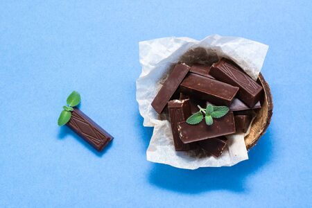 Chocolate pieces and mint leaves in a bowl and on blue paper background. The concept of overweight from sweets. Top viewの写真素材