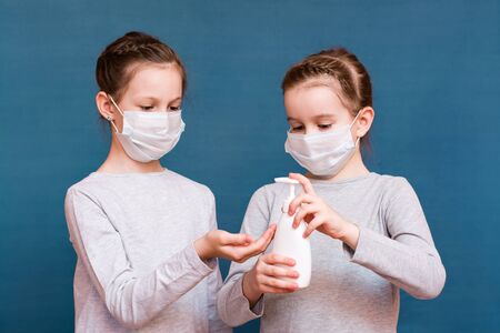 Covid-19 epidemic. Girls in medical masks treat their hands with a sanitizer on a blue background.の写真素材