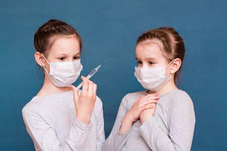 Girls in medical masks look at a syringe with medicine in their hands and are afraid. Vaccination, treatment of children. Outbreak Preventionの写真素材