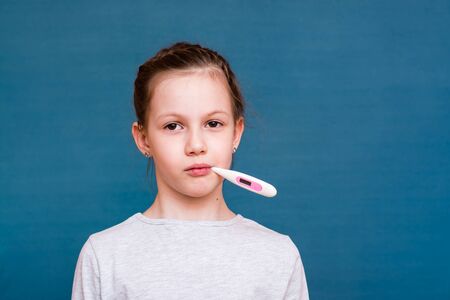 Portrait of a girl with a thermometer to measure the temperature in her mouth. Treating childrenの写真素材