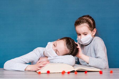 A girl in a medical mask in quarantine sleeps on a book, and another girl in a mask is afraid of the...