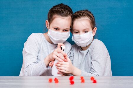 Epidemic covid-19. Girls in medical masks are protected by a sanitizer from coronavirus on a blue...
