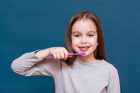 Girl wants to brush out dropping milk teeth on a blue background. The concept of oral hygiene and milk teeth in childrenの写真素材