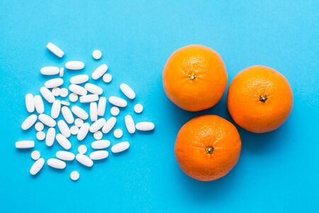 White large oval pills and ripe oranges on a blue background. Medicines and synthetic vitamins. The concept of choosing medicines and natural fruits. Top viewの写真素材