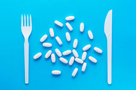White oval pills and knife with a fork on a blue background. Top view. Uncontrolled use of drugs in large quantities.の写真素材