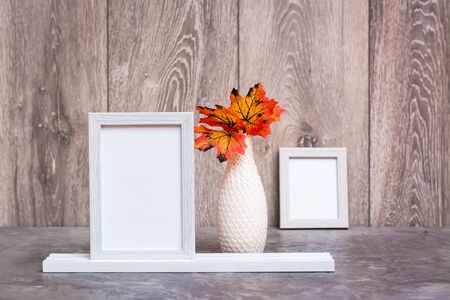 Ready Mock up. Two empty photo frames on a stand and a vase with orange maple leaves stand on the table. White-orange-beige color scheme. Copy spaceの写真素材