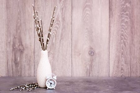 Autumn still life. A vase with willow branches and a white alarm clock stand on the table. White-gray-beige color scheme. Copy spaceの写真素材