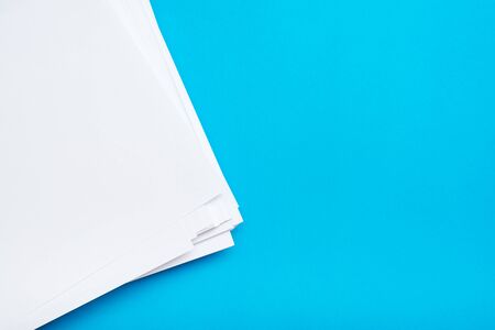 A stack of clean white paper on a table on a blue background. Blank pages ready for printing and...