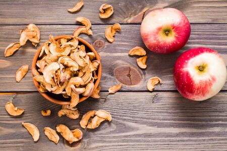 Sliced dried apples ready to eat in a bowl and fresh apples on a wooden table. Top view