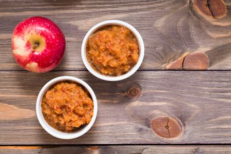 Fresh applesauce in bowls and red apples on a wooden table. Top viewの写真素材
