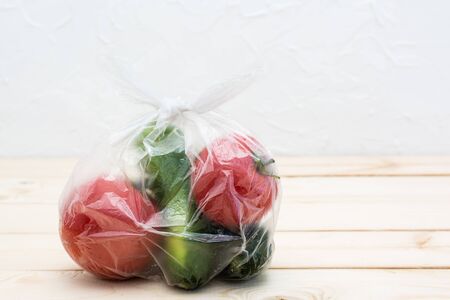 Cucumbers and tomatoes are packed in a disposable plastic bag on a wooden table. Zero Waste Conceptの写真素材