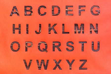 The letters of the English alphabet are carved from red cardboard, a wooden background is visible in...